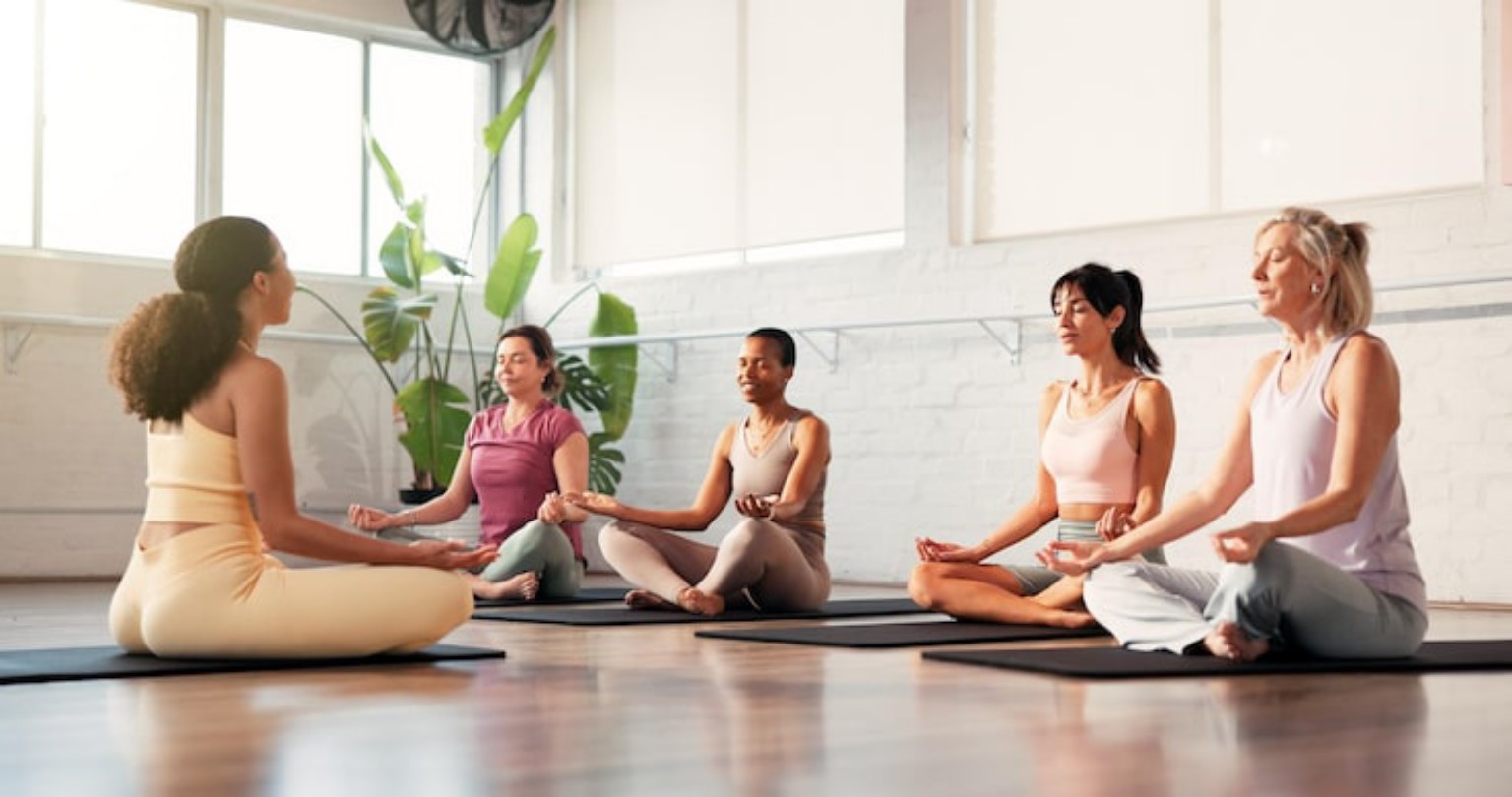 A wellness instructor guiding adult learners through a calm group meditation in a bright studio